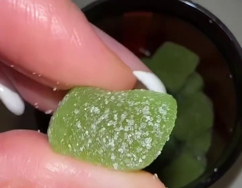 Eine Hand hält ein grünes Fruchtgummi